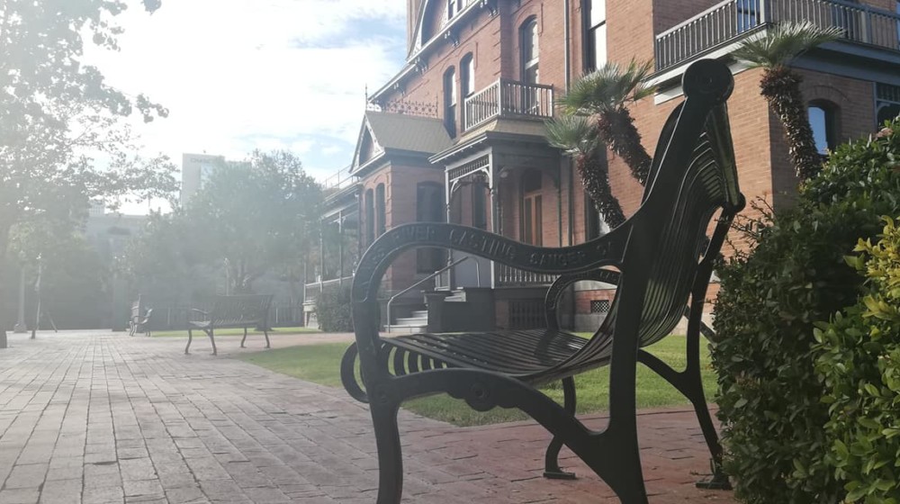 A picture of a park bench at The Square PHX with the south side of Rosson House in the background.